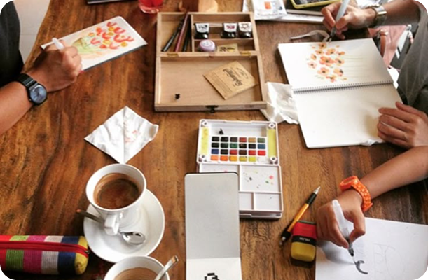 personas pintando en una mesa, con tazas de café
